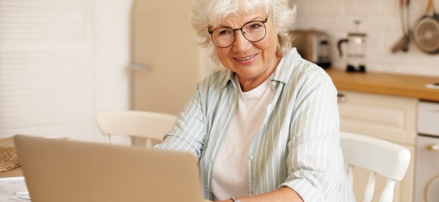 Senior woman smiling while using a laptop at home to buy Eliquis safely from Canada with a U.S. prescription.